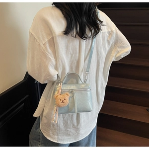 Light blue crossbody bucket bag with bear charm and silver hardware on a model