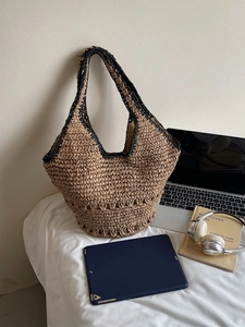 Large woven straw tote bag with black trim on white bedding with tech accessories
