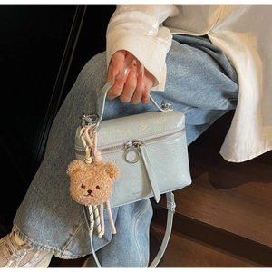 Detail of light blue glossy pleated leather bucket bag with cute brown bear charm