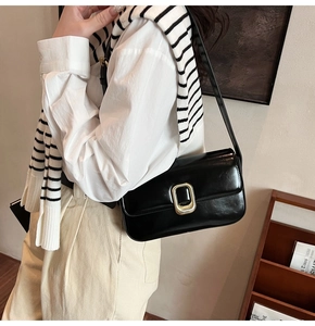 Primer plano del bolso de hombro negro con una hebilla rectangular dorada y pulida