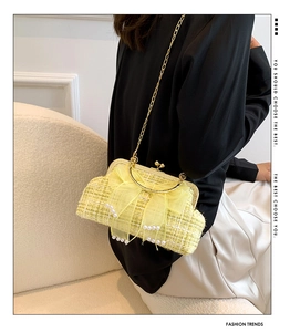 Detail of woven tweed shell bag with pearl bow and gold chain on model's side