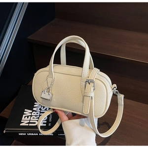 Macro detail of cream-colored pebble leather boston bag with silver lock charm