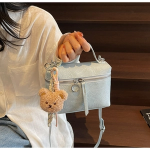 Detail of light blue textured leather crossbody bag with brown plush bear charm and silver zipper