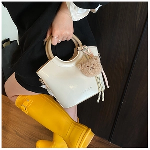 Detail of cream patent leather bucket bag with round handle and plush bear charm