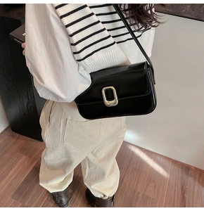 Detalle de un bolso de hombro en charol negro con una hebilla metálica rectangular dorada