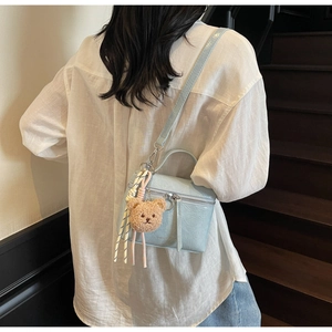 Detail of light blue crackle texture crossbody bag with cute plush bear charm on a model