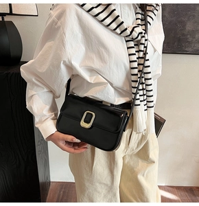 Detalle de un bolso cuadrado negro minimalista con hebilla dorada en una modelo