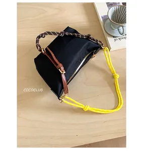 Detail of black nylon shoulder bag with yellow woven strap on a wooden desk with a coffee cup