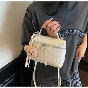Detail view of cream square handbag with pleated texture and cute brown bear charm