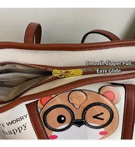 Detail of smooth golden zipper and cute bear print on beige lychee leather tote bag