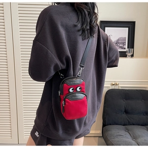 Detail showing the red canvas crossbody phone bag with double zippers and eye embroidery