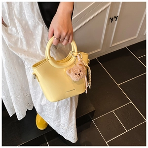 Detail of bright yellow bucket bag with plush bear charm and woven rope handle