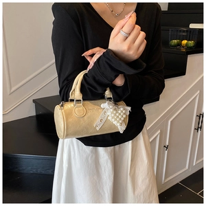 Detail of cream cylindrical bag featuring pleated texture and a pearl bow charm decoration