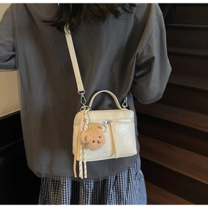 Creamy white crossbody bucket bag with glossy texture and cute plush bear charm decoration