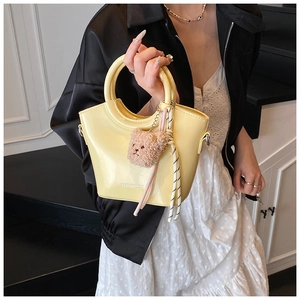 Detail of yellow patent leather bucket bag with wavy rim, bear charm and striped ribbon