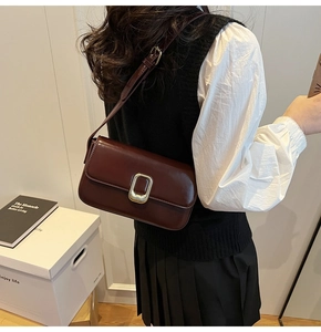 Detalle de bolso bandolera de cuero burdeos con hebilla dorada y un diseño elegante