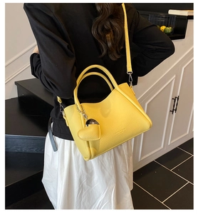 Model showing a yellow lychee leather handbag with heart pendant and FASHION lettering