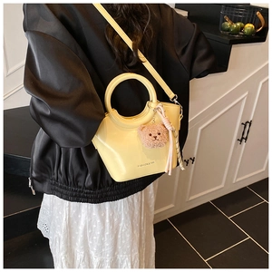 Detail of light yellow bucket bag with metal ring handle and plush bear charm