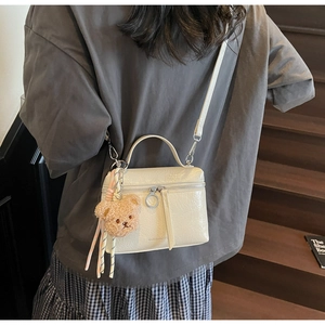 Detail of cream pleated crossbody bucket bag with teddy bear charm and brand logo