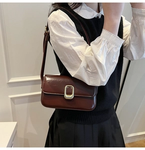 Detalle de bolso bandolera marrón oscuro con hebilla dorada en una modelo