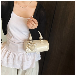 Close-up of white cylindrical handbag featuring pearl heart charm and ribbon bow detail