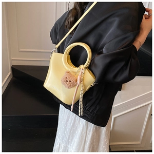 Detail of pale yellow glossy bucket bag with metal ring handle and cute bear charm