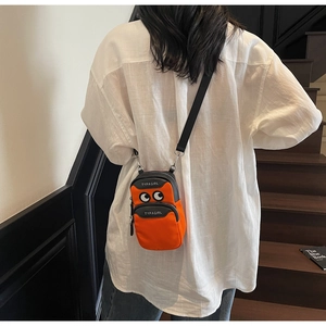 Orange crossbody phone bag with cartoon eyes detail worn by model on stairs