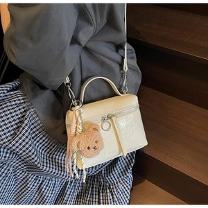 Detailed close-up of cream white crackle pattern handbag with cute bear charm on steps