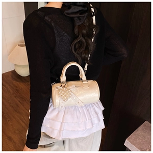 Detail of retro cylinder bag in cream patent leather with pearl heart and lace bow
