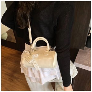 Detail of cream barrel bag with glossy wrinkled leather and pearl lace bow pendant