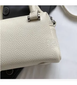 Close-up of beige litchi grain leather texture and metallic buckle on the handbag