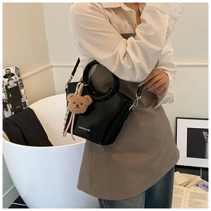 Detail of black patent leather bucket bag with metal handle and plush bear charm