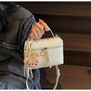 Close-up of white bucket bag with pleated texture and cute brown plush bear charm