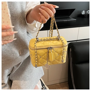 Detail of yellow quilted leather box bag with silver studs and chain strap held by a person