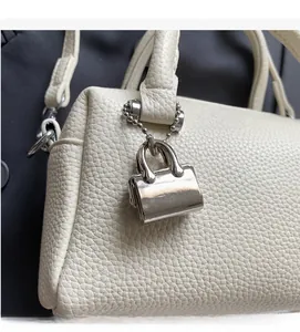 Detail of off-white lychee texture handbag with a silver metal bag-shaped charm