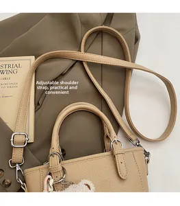 Detail of beige lychee leather handbag with adjustable strap and plush bear charm decoration