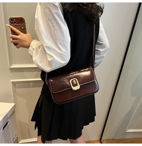 Detalle de bolso de hombro en cuero brillante marrón oscuro con hebilla ovalada dorada