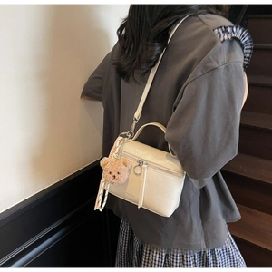 Detail of cream crossbody bucket bag with plush bear charm on soft leather texture