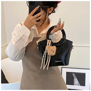 Detailed close-up of glossy black bucket bag with ring handle and cute bear charm