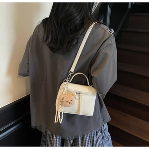 Detail of cream glossy wrinkled leather bucket bag with cute bear charm and shoulder strap