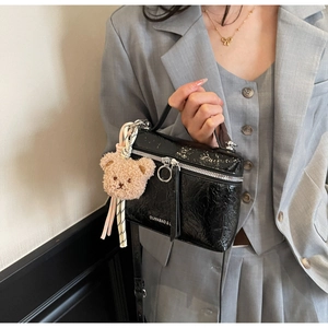 Detail of black wrinkled patent leather handbag with silver ring zipper and bear charm