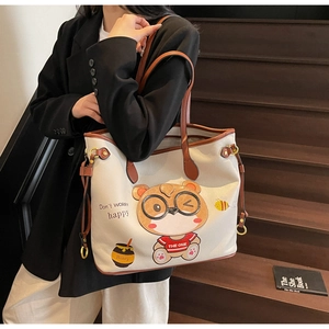 Close-up of cream tote bag with cute cartoon bear print and brown leather handles