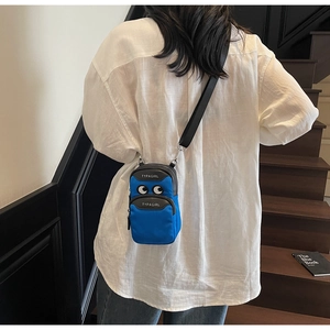 Blue nylon crossbody phone bag with cartoon eyes shown on a model in a casual setting
