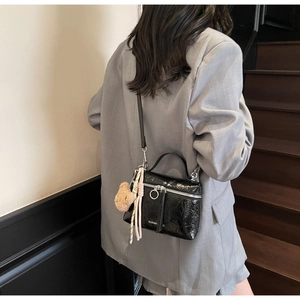 Detailed view of black pleated crossbody bag with plush bear charm on a model