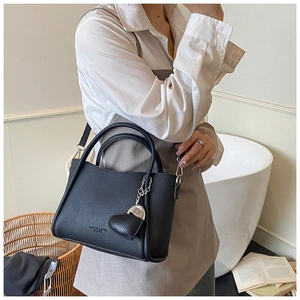 Close-up of black lychee grain leather tote bag featuring a heart pendant and silver hardware