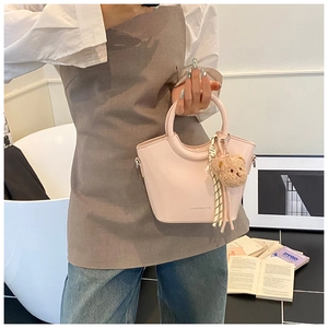 Close-up of light pink bucket bag with plush bear charm and ribbon on model's hand