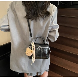 Detail of black glossy pleated bucket bag with silver ring zipper and cute bear charm
