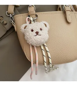 Close-up of cute plush bear charm with woven ropes on light brown leather bucket bag