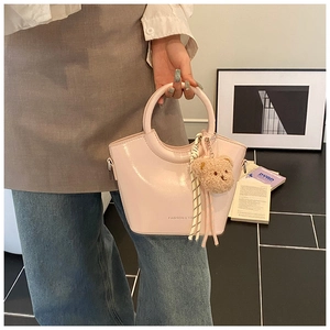 Pink patent leather bucket bag with plush bear charm and striped scarf detail in hand