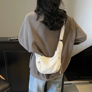 Detail view of white canvas crescent hobo bag worn crossbody by a model in casual setting